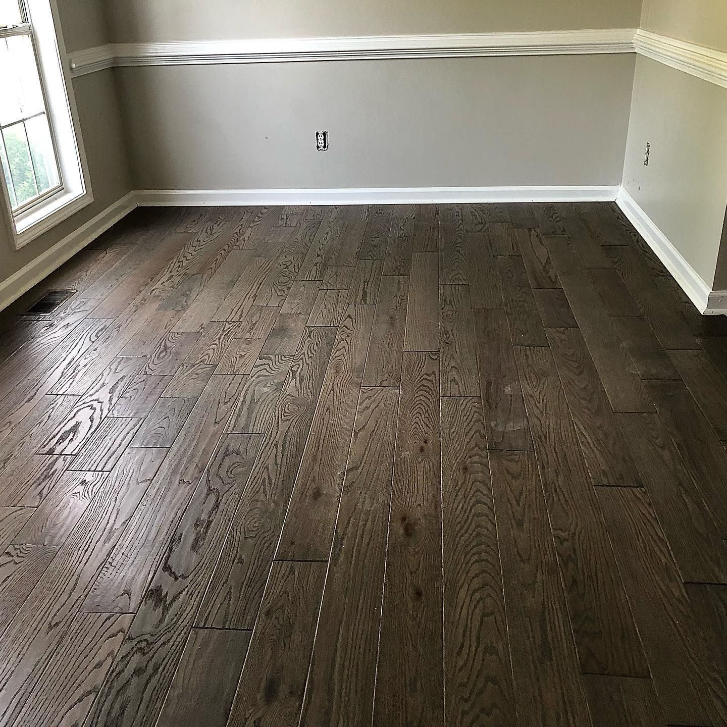 Empty room with dark hardwood floors, light gray walls, and a window on the left.