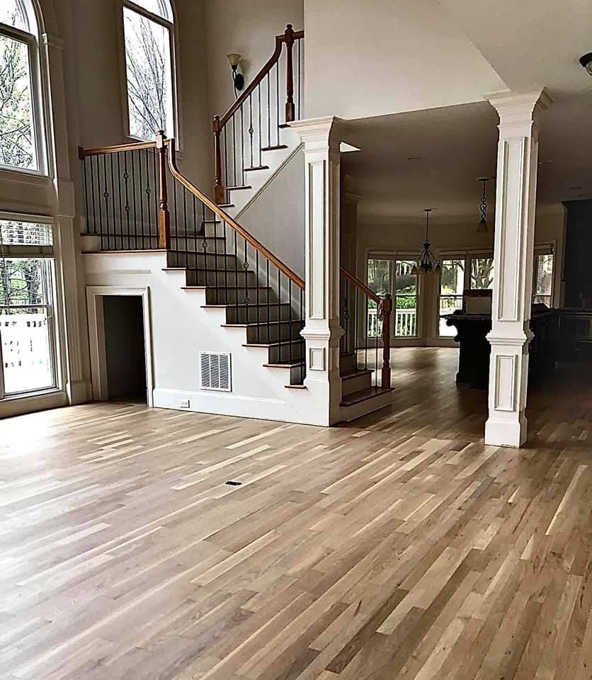 Spacious living room with hardwood floors, staircase, and tall windows in a bright open interior