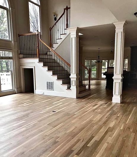 Spacious living room with hardwood floors, staircase, and tall windows in a bright open interior