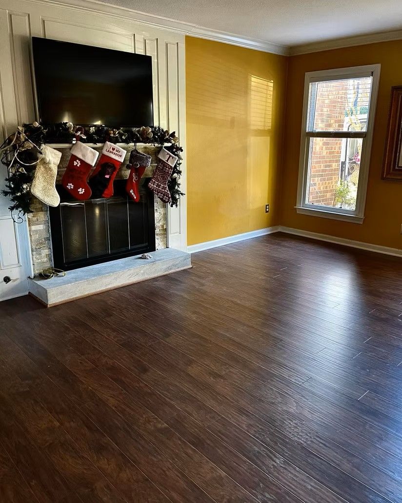 Empty living room with dark wood floors, yellow walls, a fireplace, and a window with daylight.
