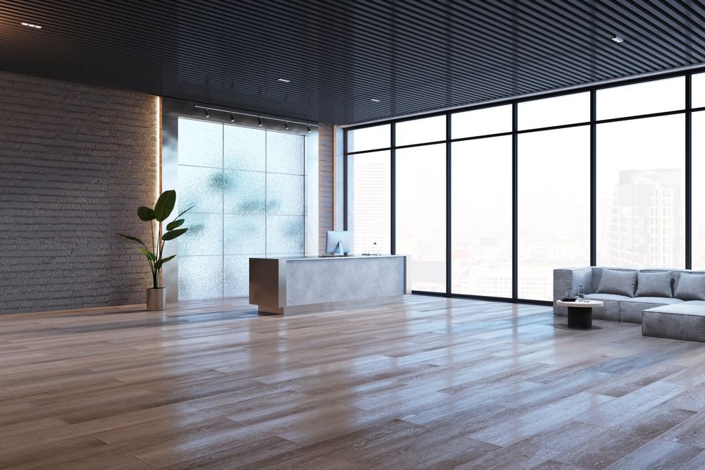Modern minimalist living room with wood floors, large windows, a sofa, plant, and white desk