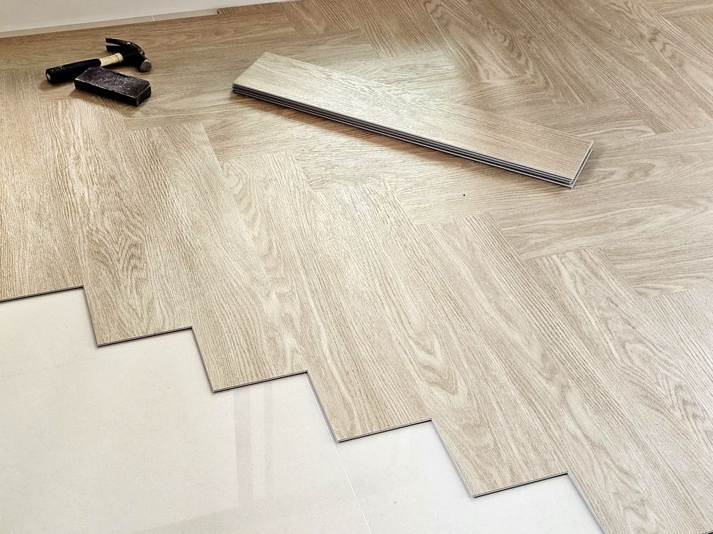 Wood-pattern flooring planks being installed, with black spacers and a saw on a herringbone-style wood floor.