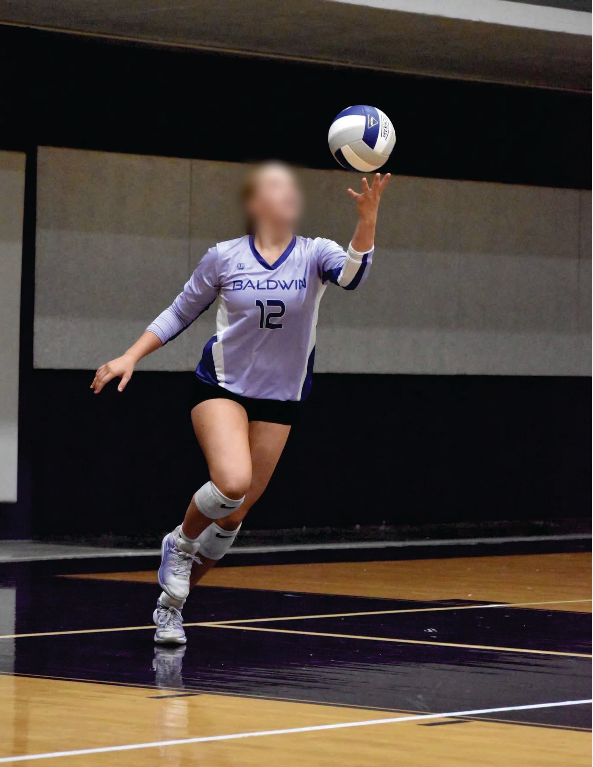 Volleyball player in a purple Liddle's jersey leaps to serve on an indoor court