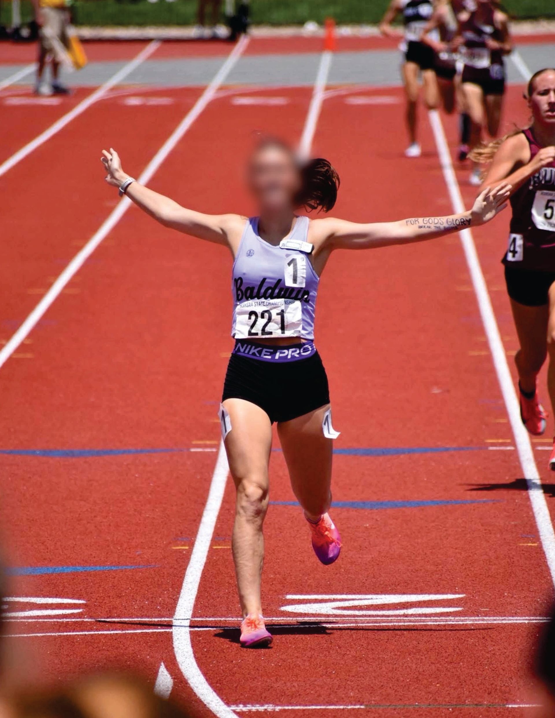 Runner crosses the finish line with arms outstretched on a red track in purple Liddle's track uniform
