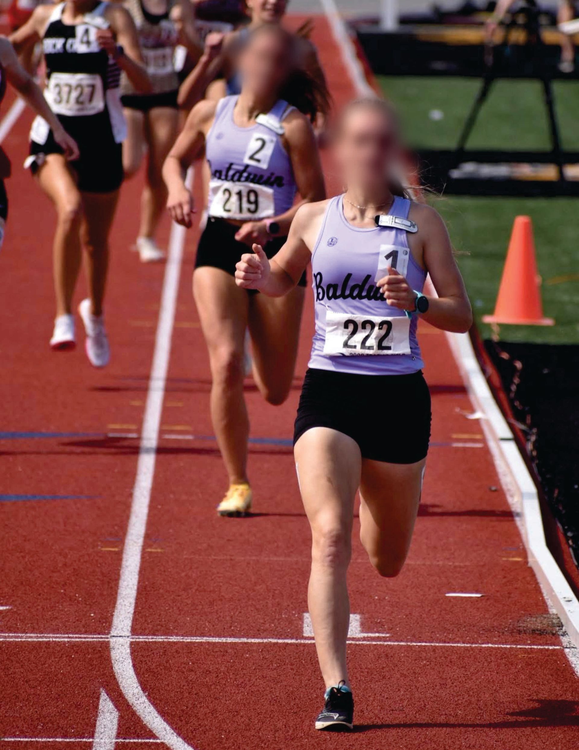 Two runners on a red track, one leading with a race bib and purple Liddle's track uniform