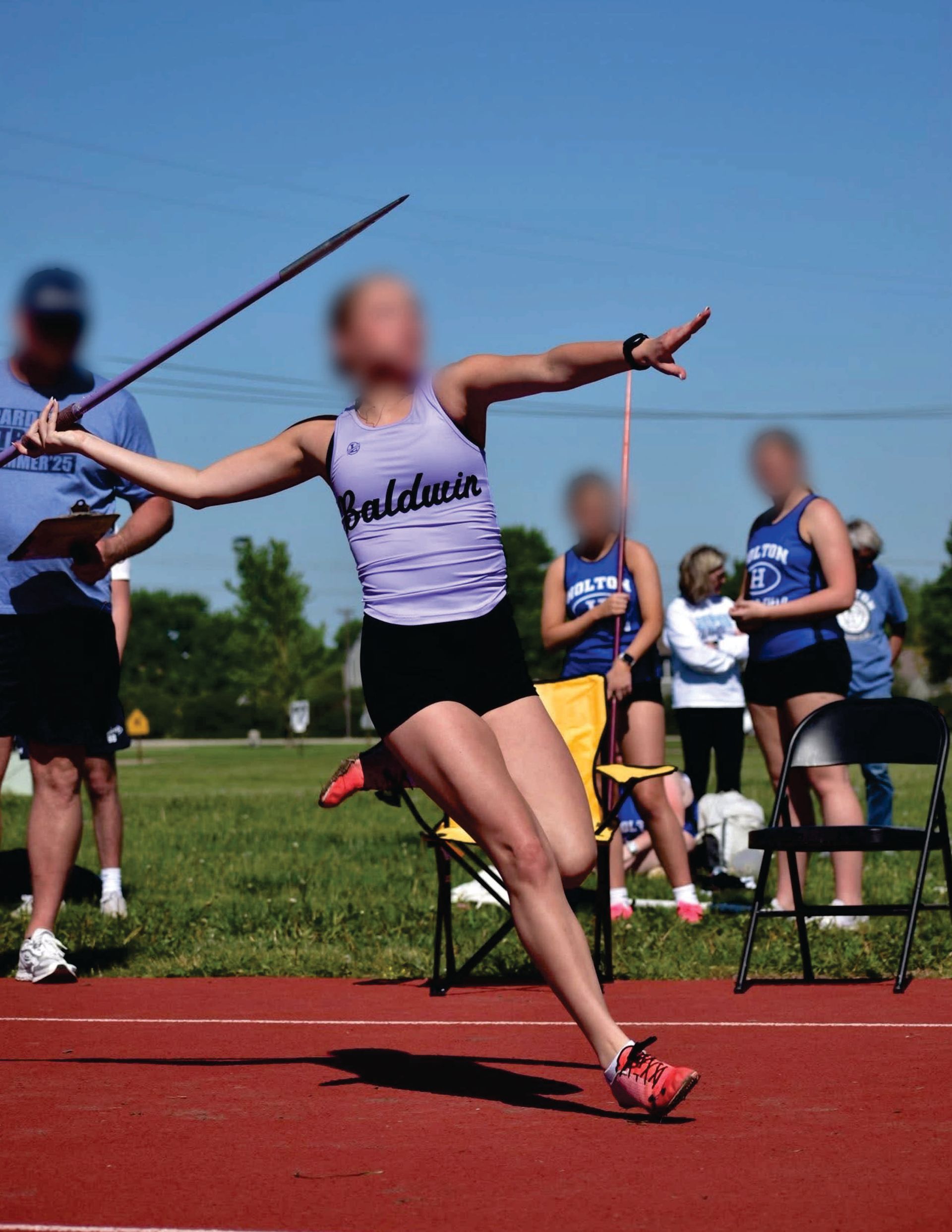 Athlete in purple Liddle's uniform throws a javelin on a track, with competitors and spectators in the background.