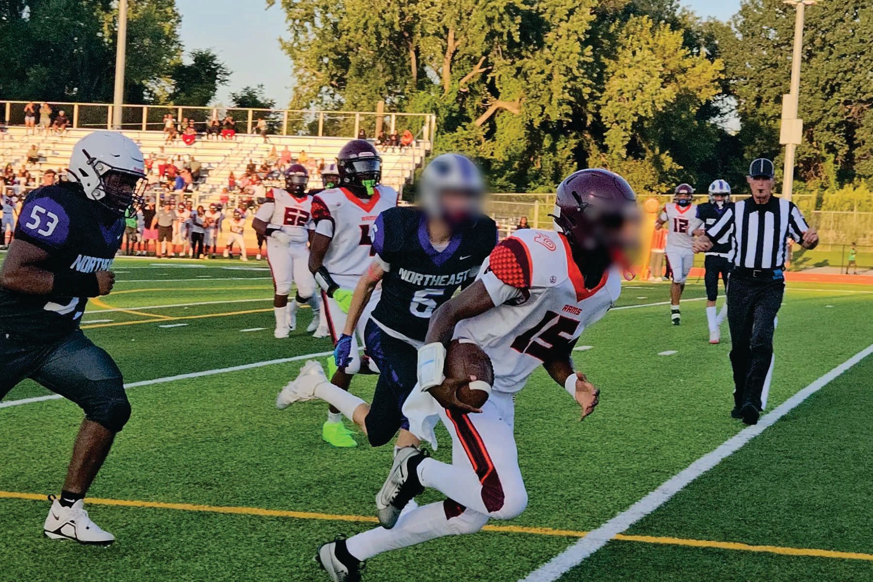Football player in white Liddle's uniform runs with the ball as defenders chase on a field at sunset
