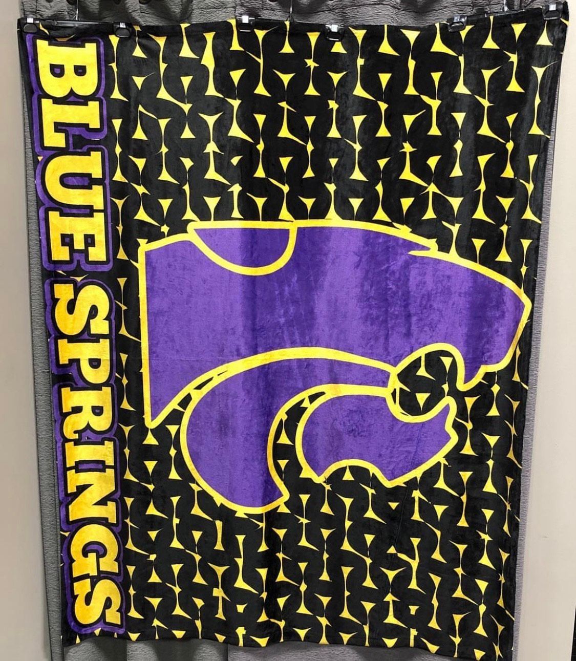 Blue Springs Wildcats blanket: purple logo on black and yellow patterned background; vertical