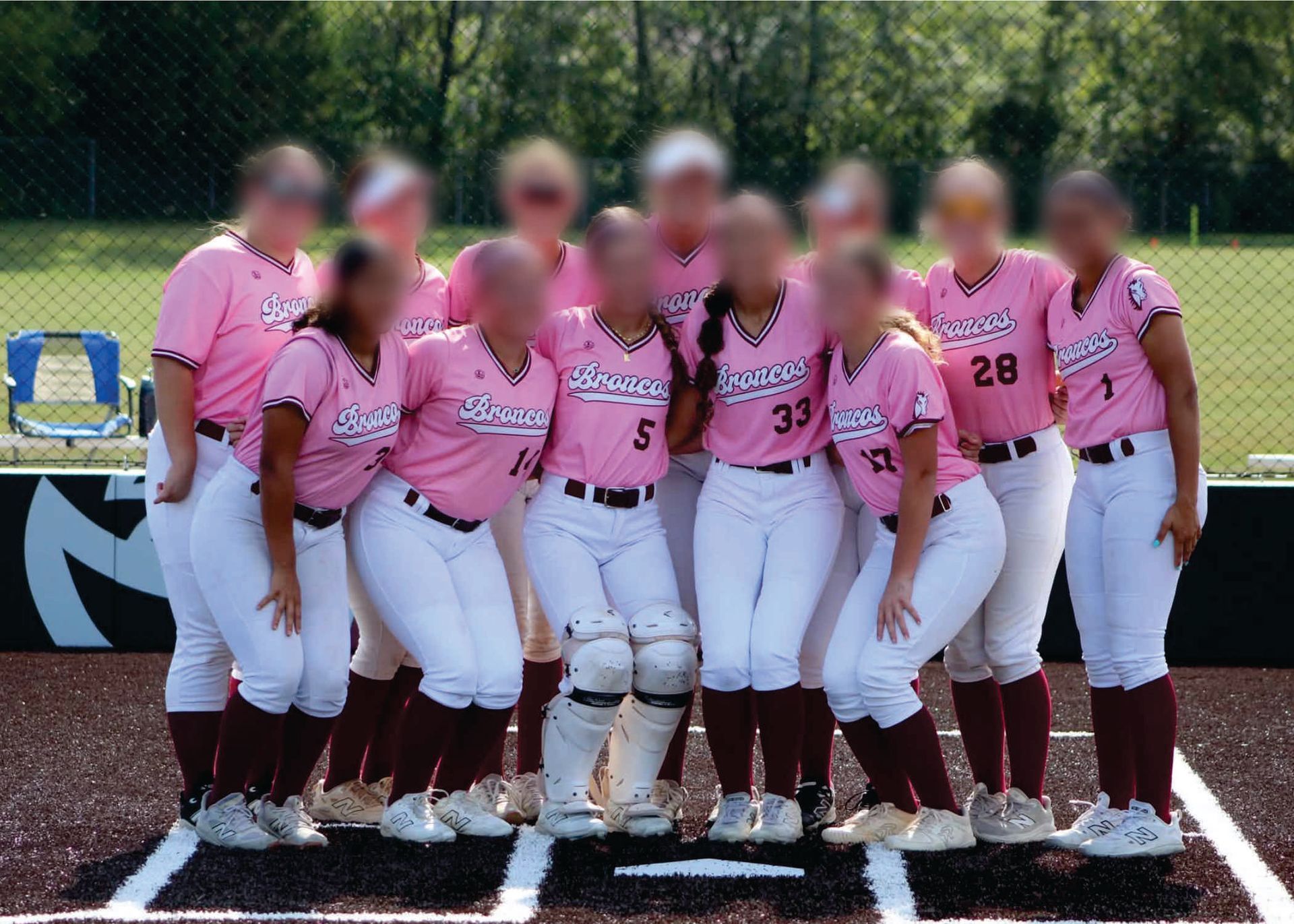 Softball team in pink Liddle's  jerseys posing on a field after a game, with bats and dugout in the background