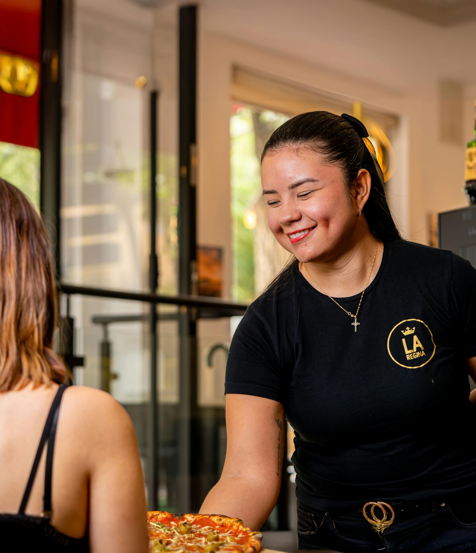 Server smiling, delivering pizza to a customer in a restaurant.