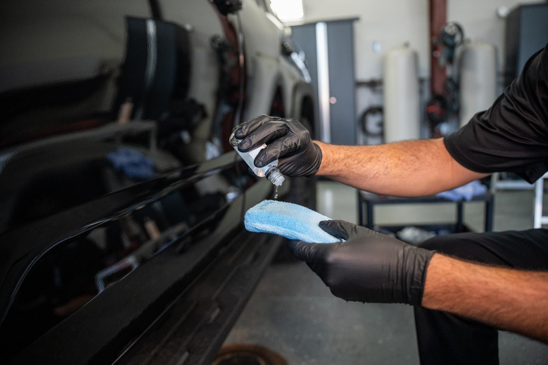 Person in black gloves applying a liquid to a car panel with a blue applicator.