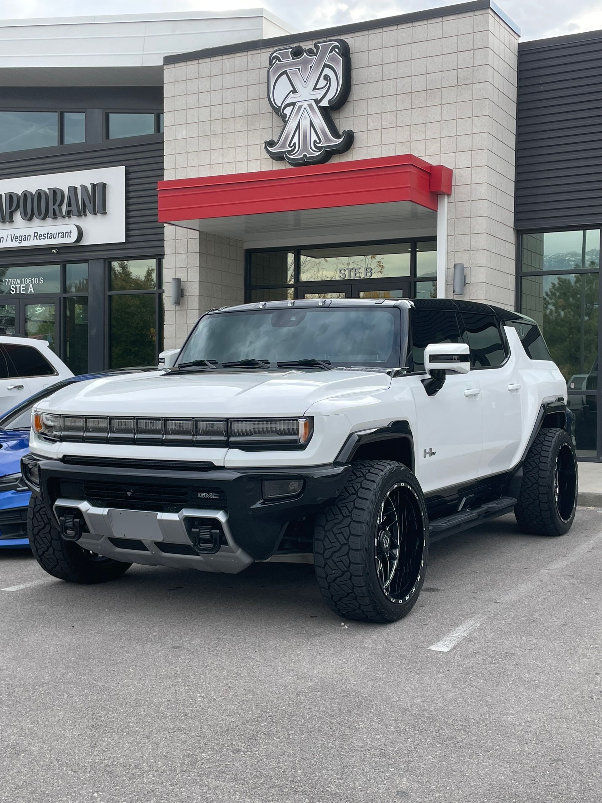 White Hummer EV with black accents parked in front of a building with a red awning.