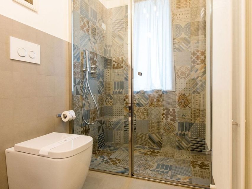 Bagno con doccia a fantasia, WC e pareti grigio chiaro.