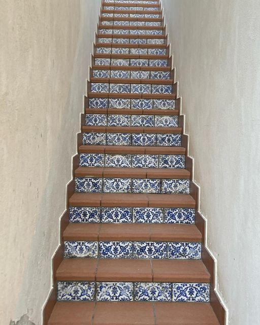 Scala con gradini marroni e piastrelle a motivi blu. Le pareti beige incorniciano la scala, che sale verso l'alto.