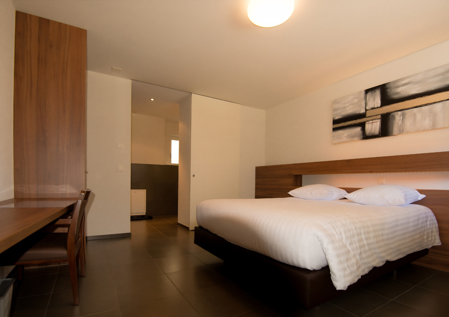 Chambre d'hôtel moderne avec lit, bureau, armoire et décorations murales dans une ambiance chaleureuse.
