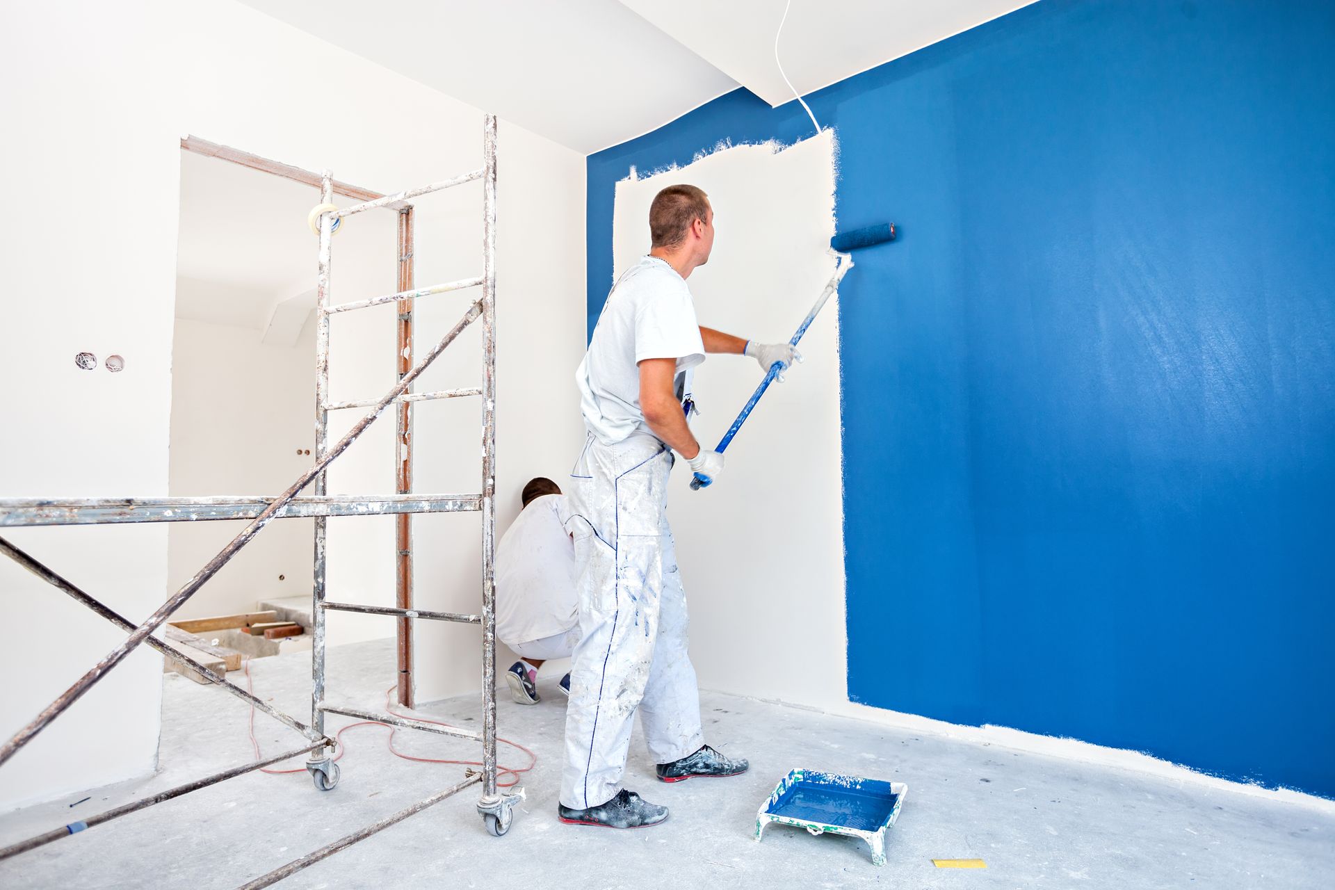 A man is painting a blue wall with a roller.