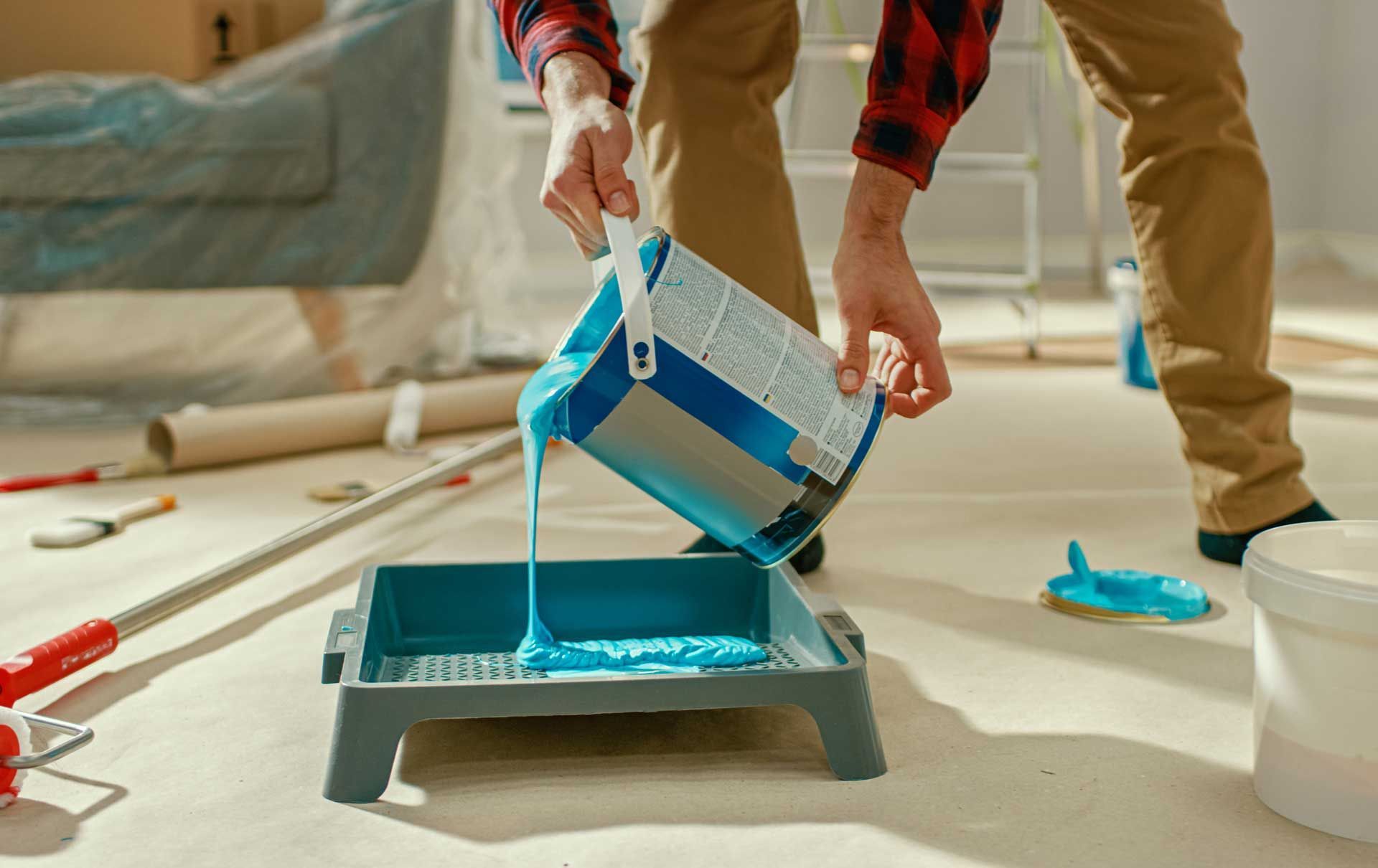 A man is pouring blue paint into a paint tray.