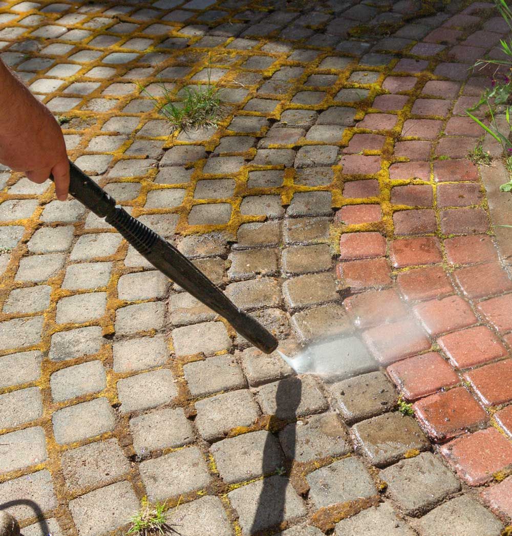A person is cleaning a brick walkway with a high pressure washer.