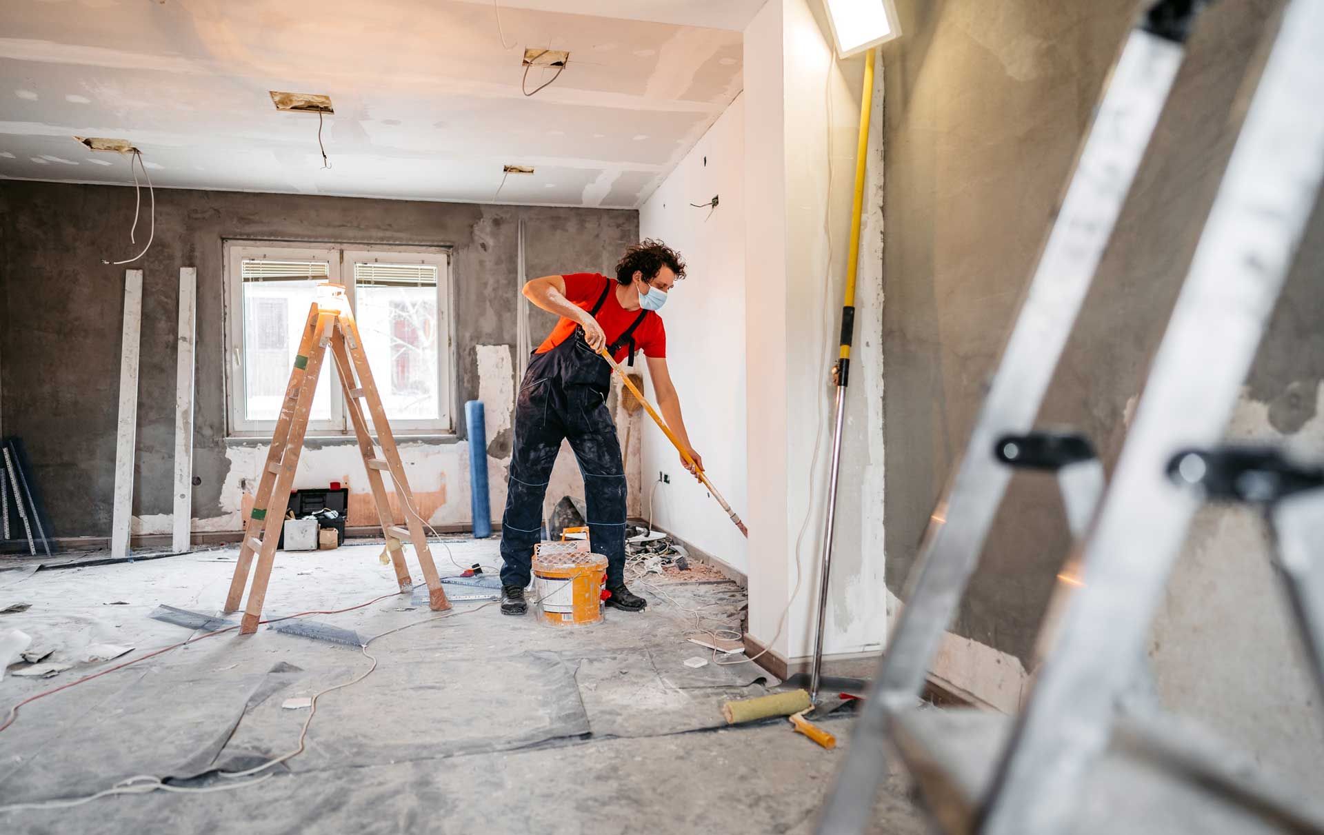 A man is painting a wall in a room while wearing a mask.
