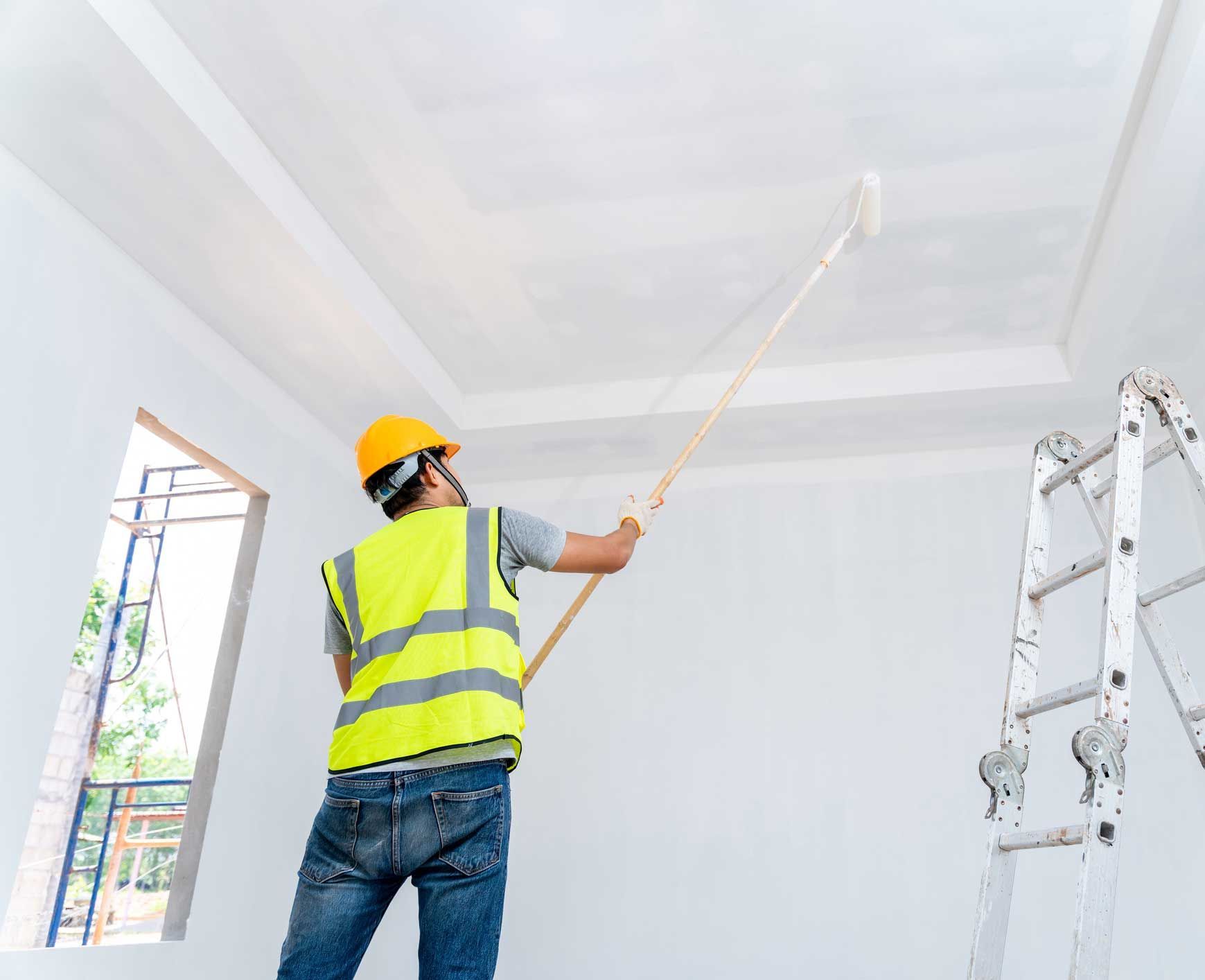 A man is painting the ceiling of a room with a paint roller.