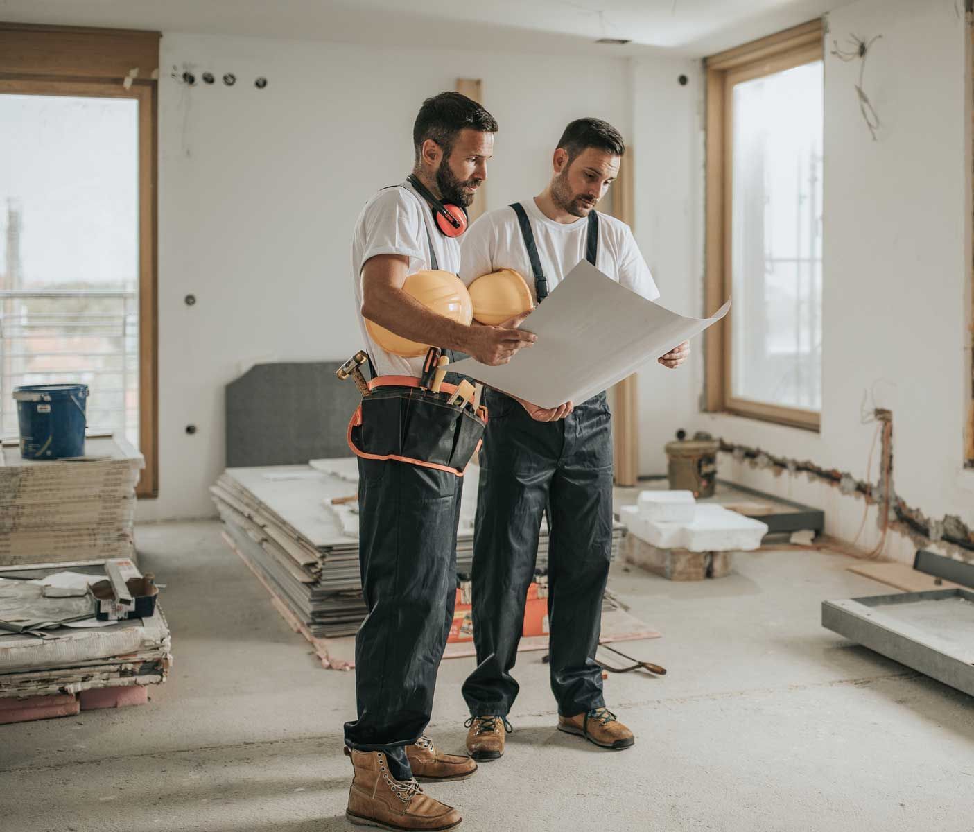 Two men are standing in a room looking at a blueprint.