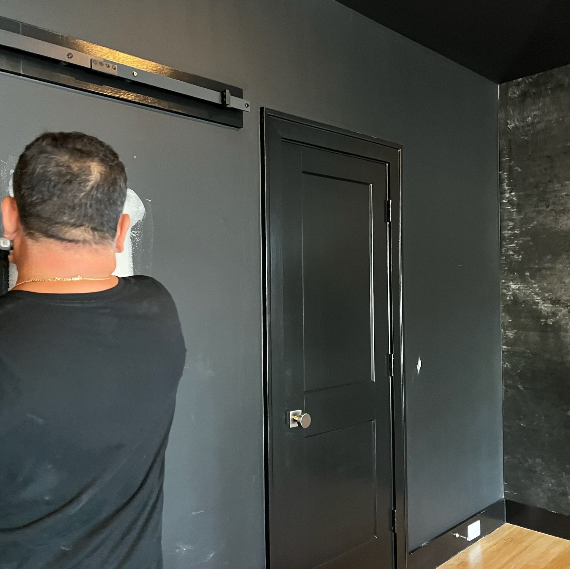 A man in a black shirt is standing in front of a black door