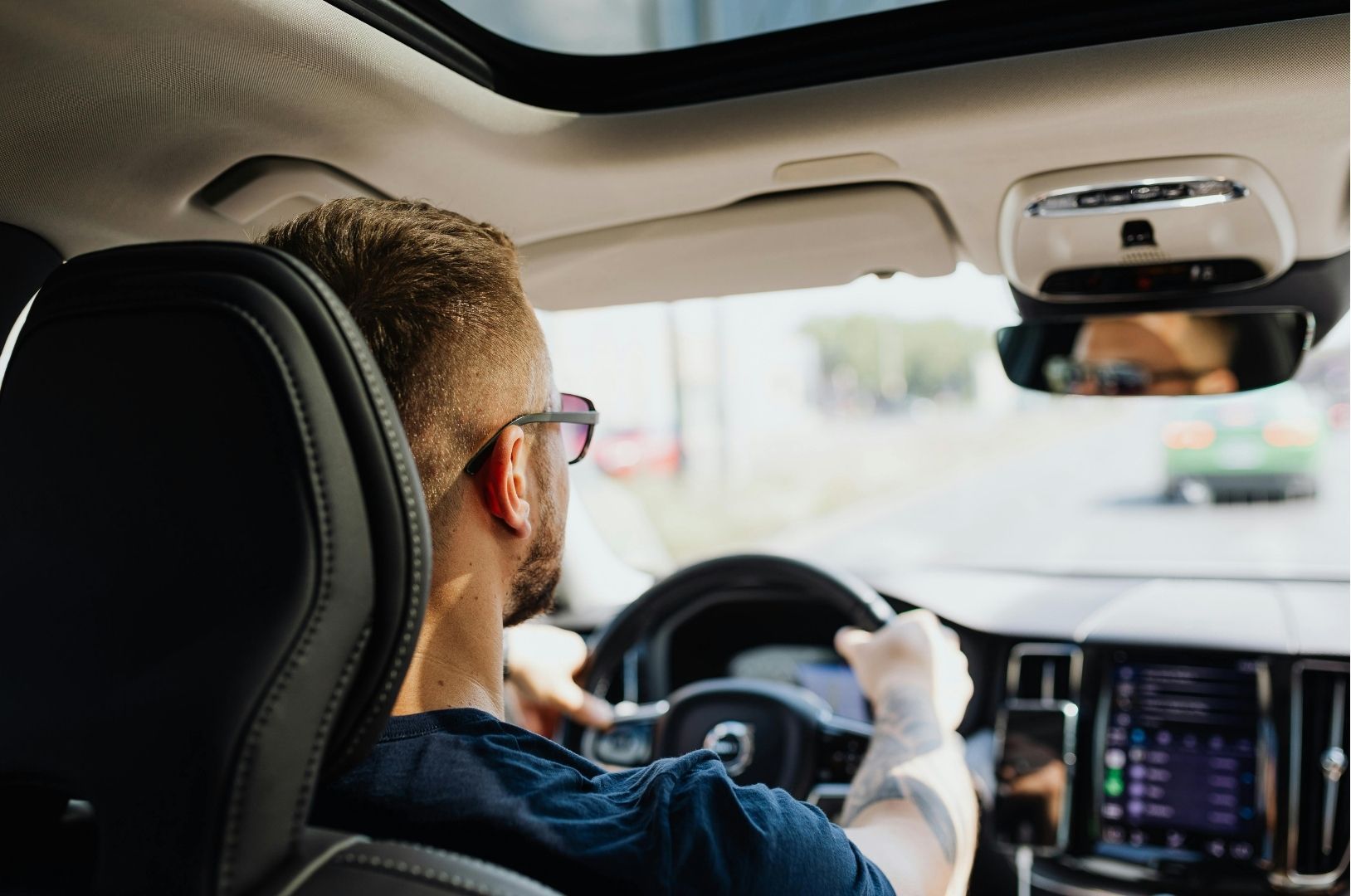 Driver holding the wheel in a modern car interior, with a bright road visible ahead.