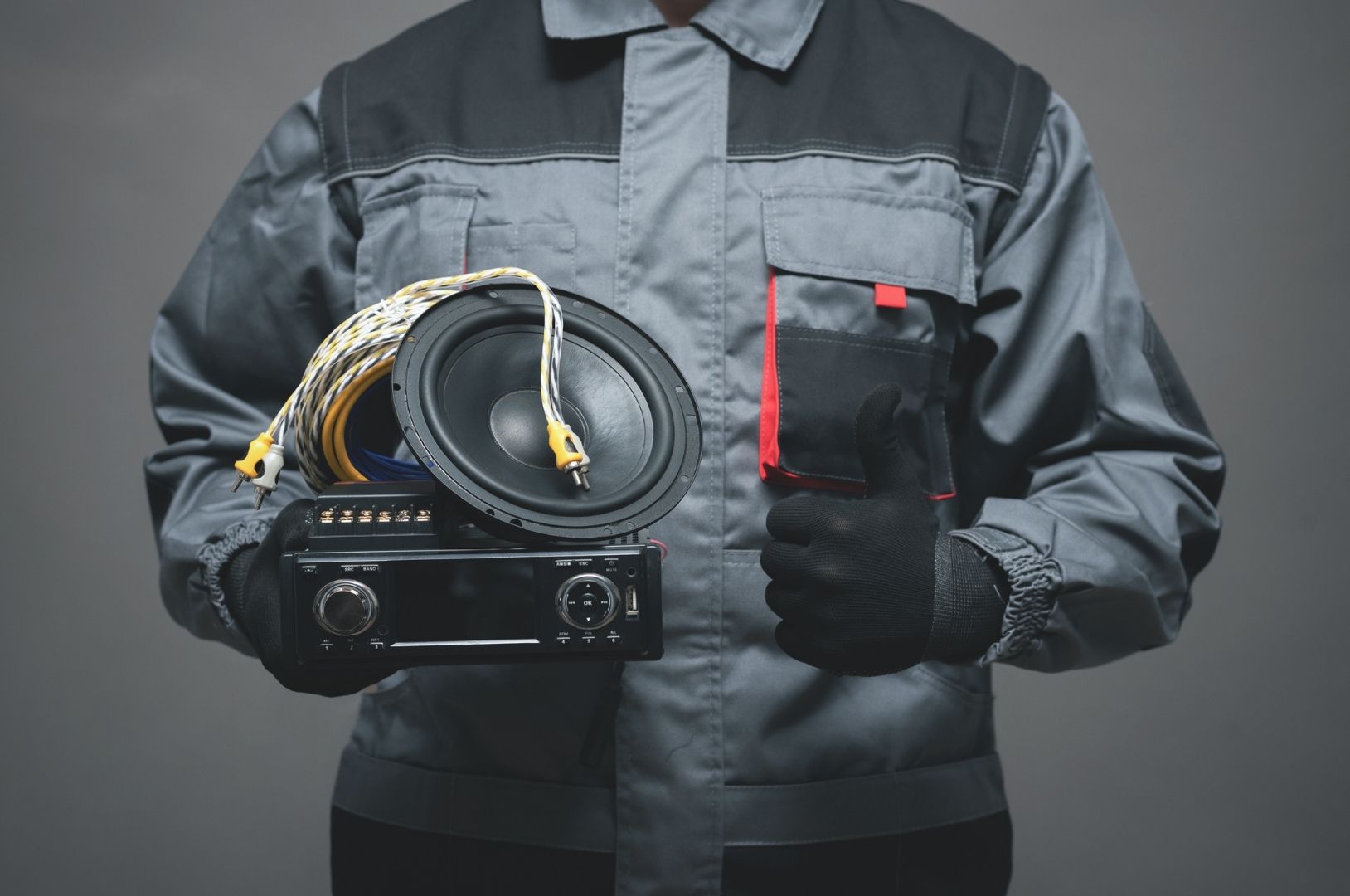 Person in gray work jacket holding a coiled cable and a black device with red accents against a dark background