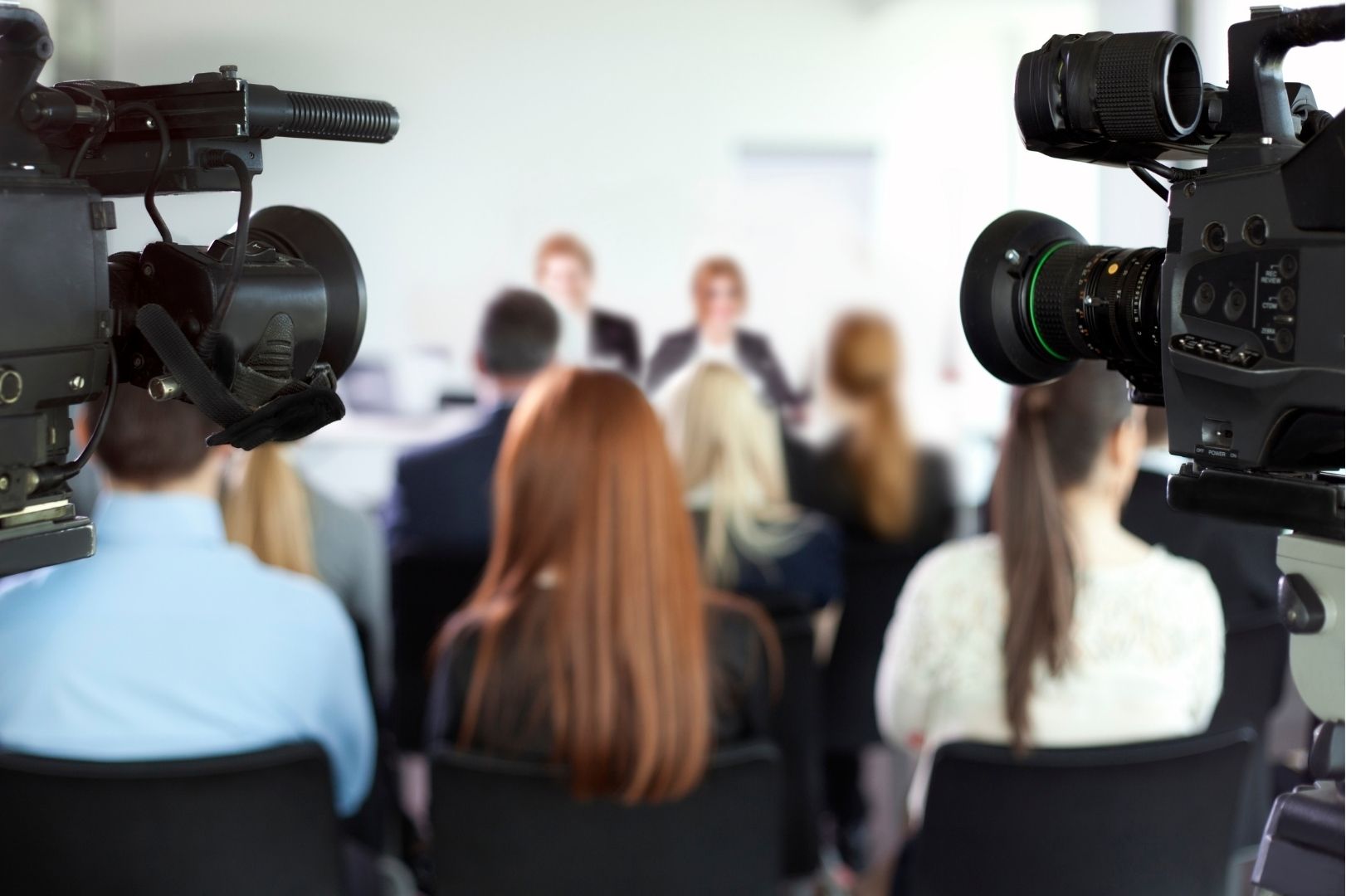 Cameras filming an audience at a conference or presentation in a bright meeting room