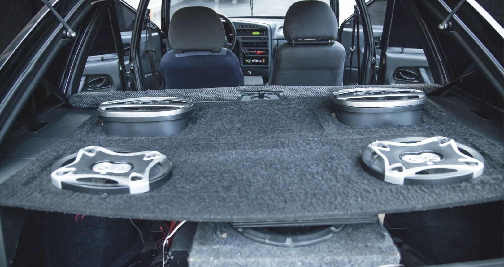 Car trunk with a large black cargo shelf and two silver speaker mounts, viewed from the rear seat area