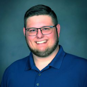 Smiling person in glasses wearing a teal shirt against a gray background