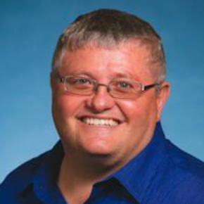 Smiling person in glasses wearing a blue shirt against a blue gradient background