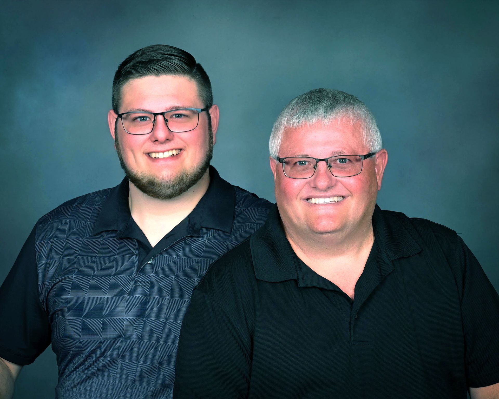 Two smiling men in black shirts posing against a blue studio backdrop