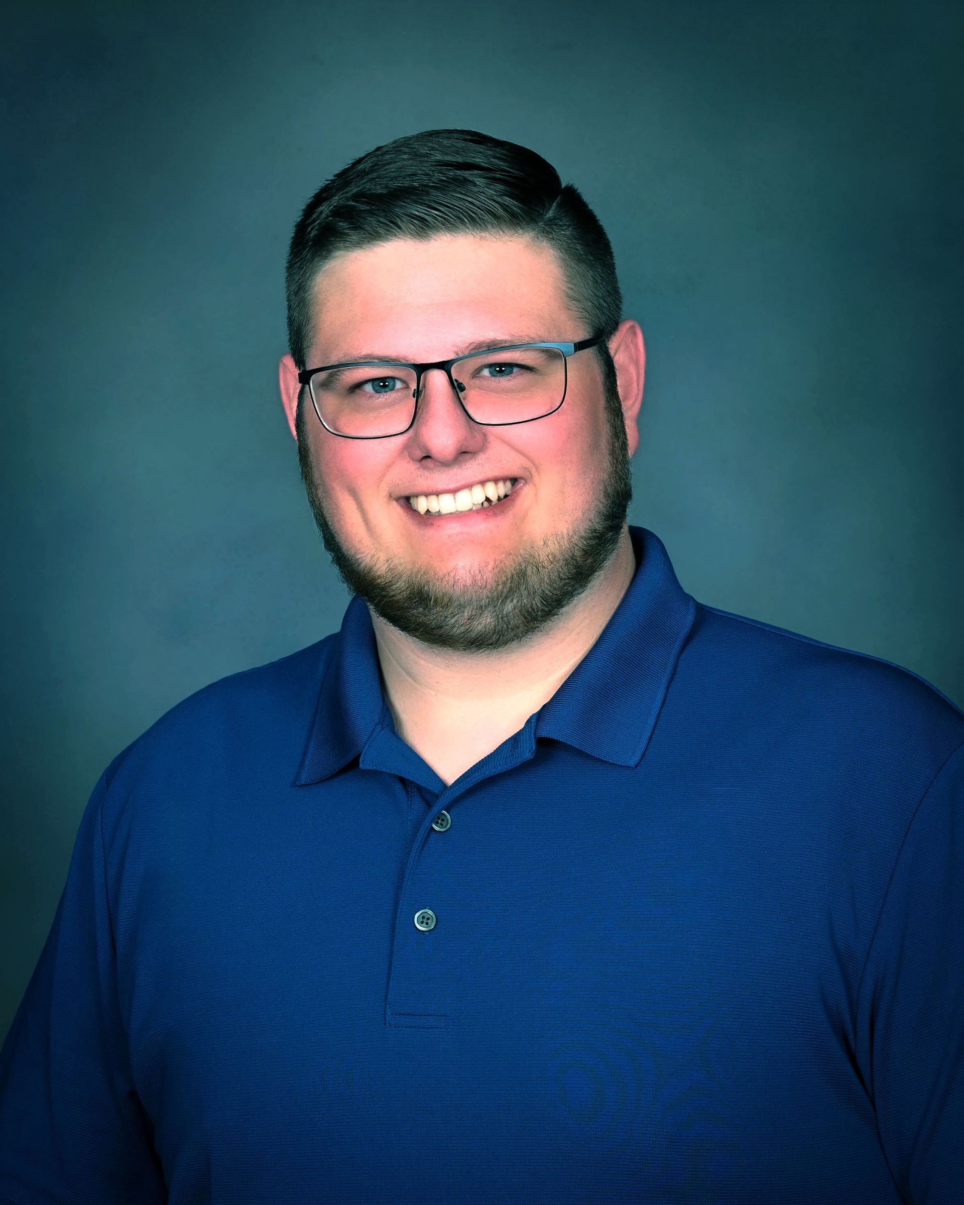 Smiling man in glasses wearing a blue shirt against a blue studio background