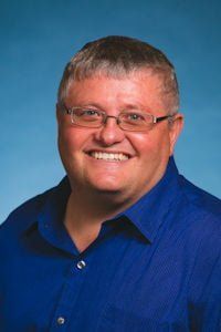 Smiling man in glasses wearing a blue shirt against a blue studio background