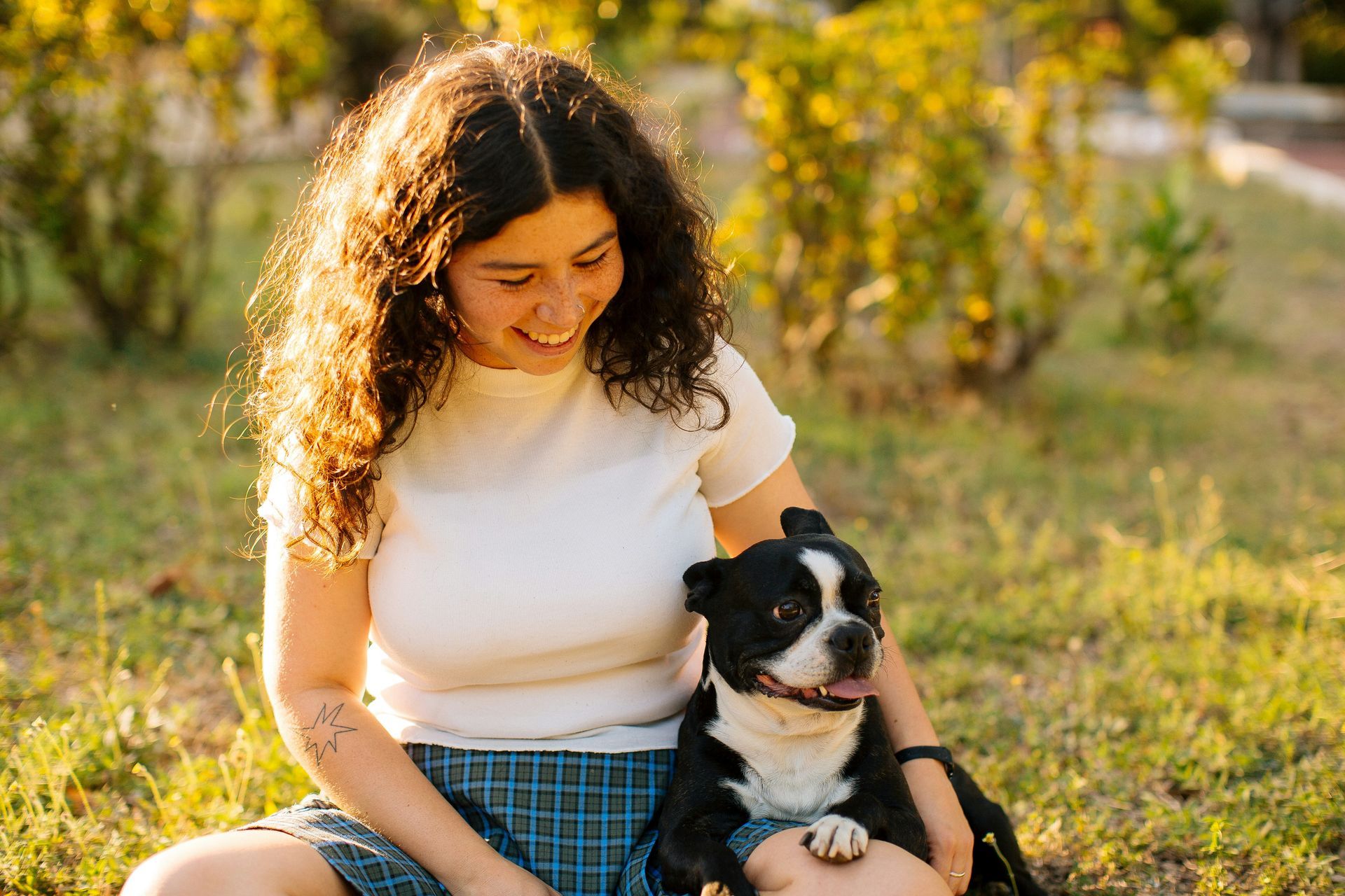 Woman in a white shirt sits with a black-and-white dog in a sunny grassy field