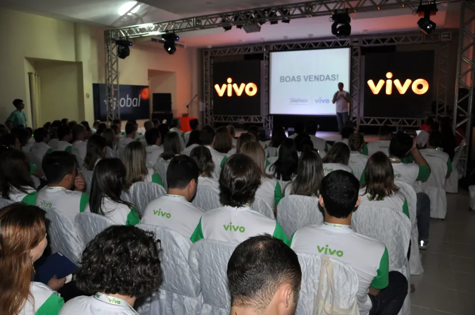 Um grande grupo de pessoas está sentado em frente a uma tela que diz vivo