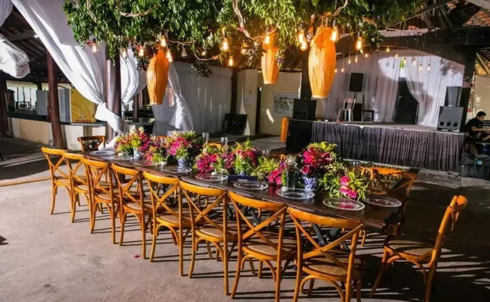 Uma longa mesa e cadeiras são colocadas para uma recepção de casamento sob uma árvore. -HOTEL-FAZENDA-PARAISO