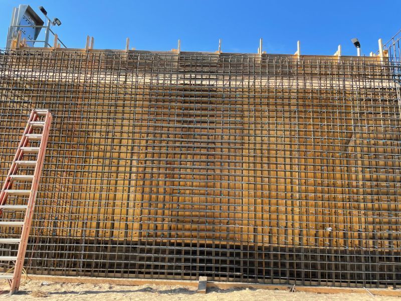 Reinforced concrete wall construction with a ladder against it and a clear blue sky.
