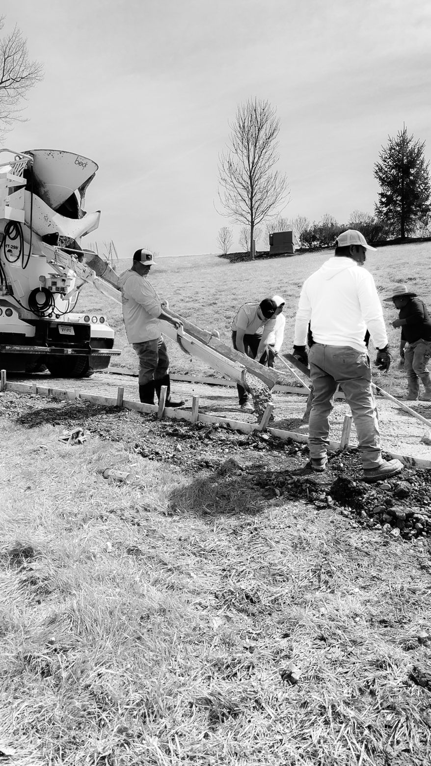 Concrete being poured by a pump truck onto a construction site. Workers wearing safety vests and helmets are present.