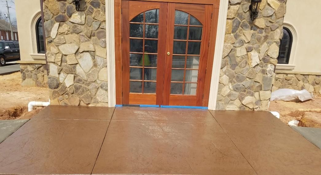 Stamped concrete patio in front of a building with stone columns. Brown and tan colors.