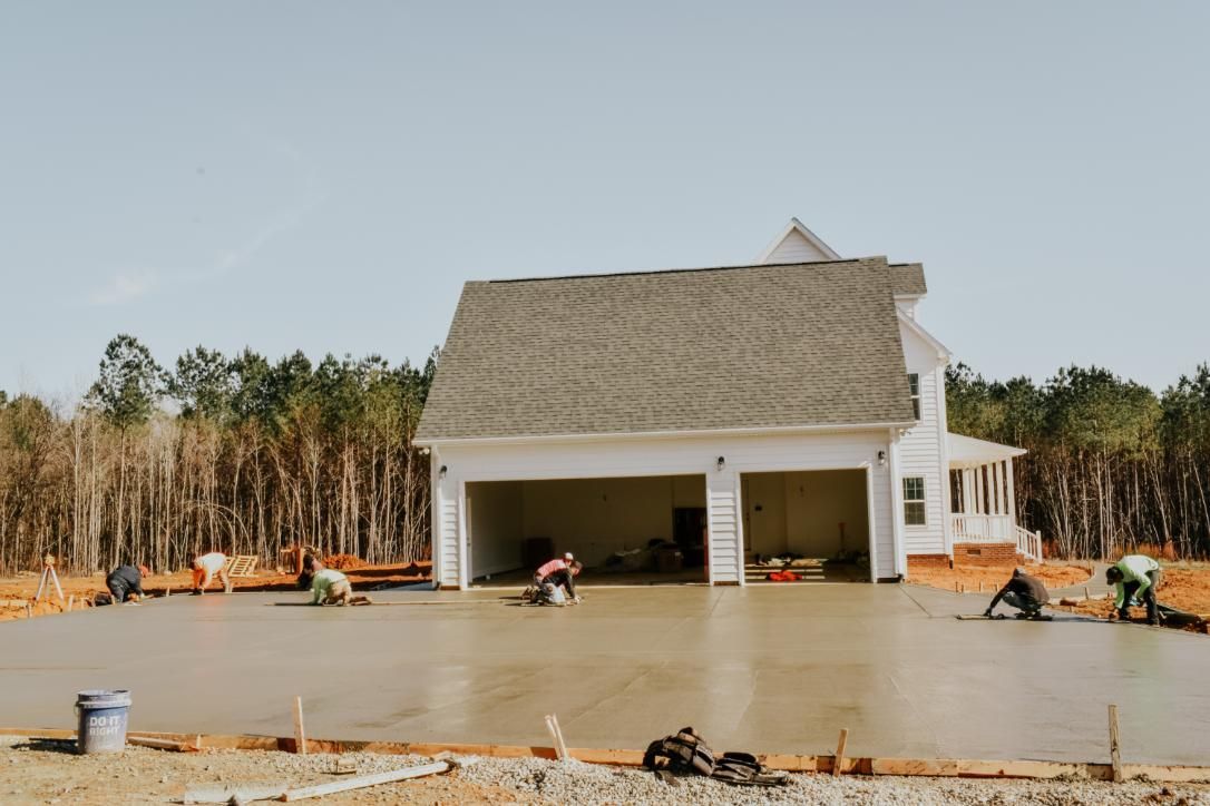 Construction workers smoothing wet concrete driveway in front of a house with a two-car garage.
