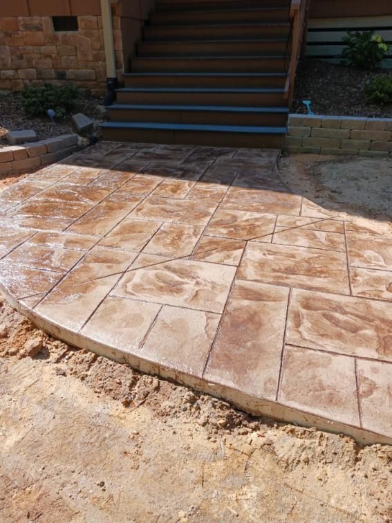 Stamped concrete patio with stone pattern leading to wooden stairs.