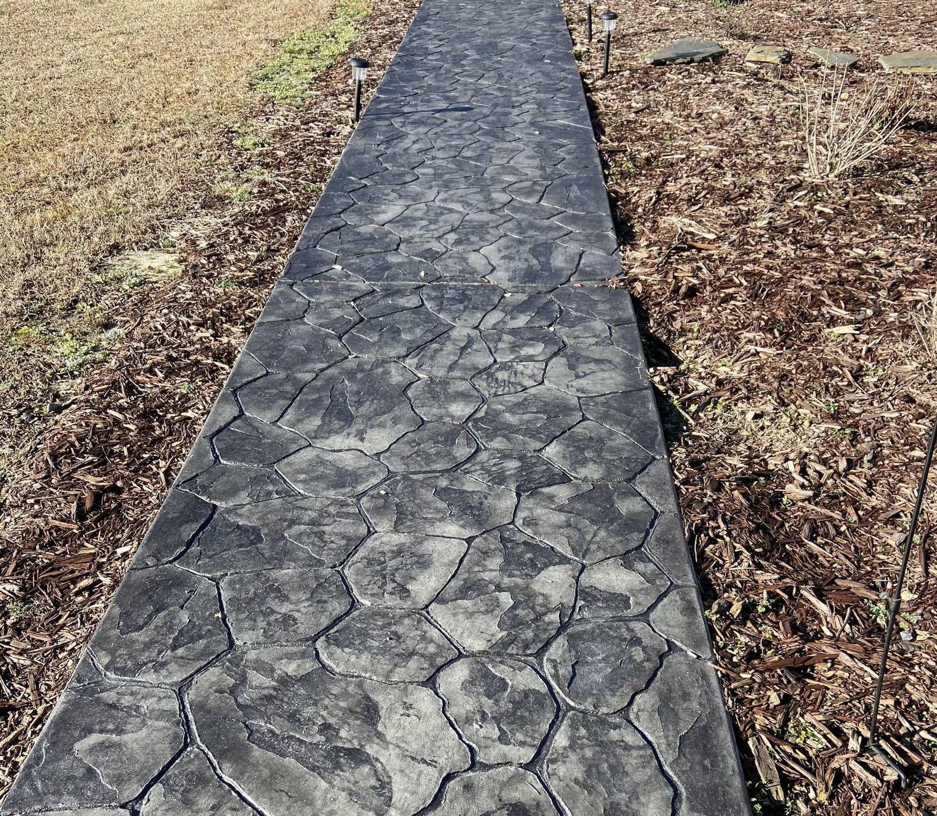 Dark gray stone-textured concrete walkway, set in a yard with brown grass and dirt.