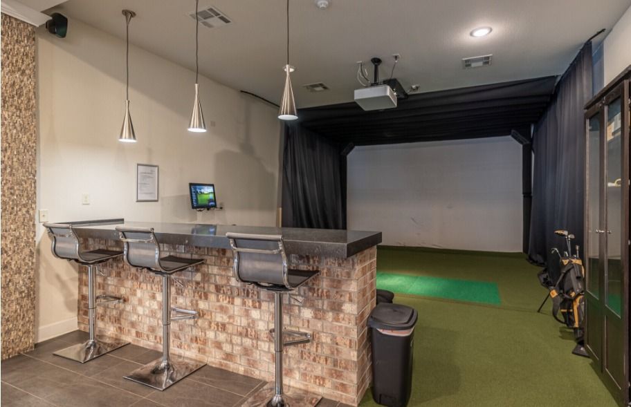 Golf simulator in front of bar seating with three stools and pendant lighting 