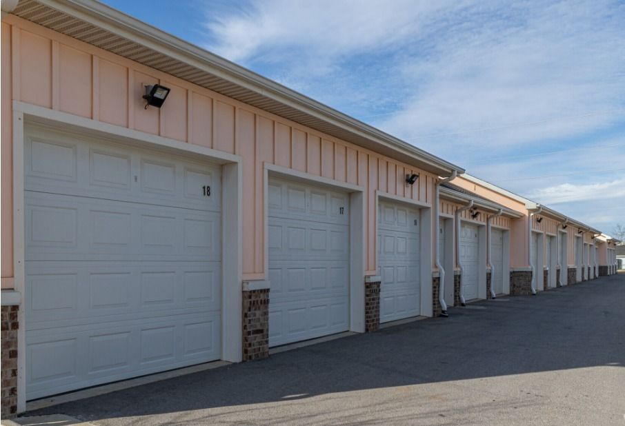 a row of detached garage parking with white doors, stone trim, and beige wooden siding