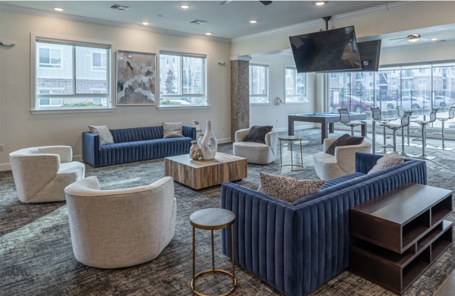 Centerton clubhouse with large blue couches, white armchairs, and a large TV mounted hanging from the ceiling.