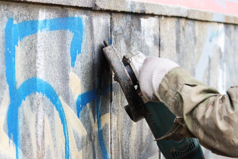 A Person is Using a Grinder to Remove Graffiti From a Wall — D & J Saverino Painting & Decorating Pty Ltd In Fairy Meadow, NSW