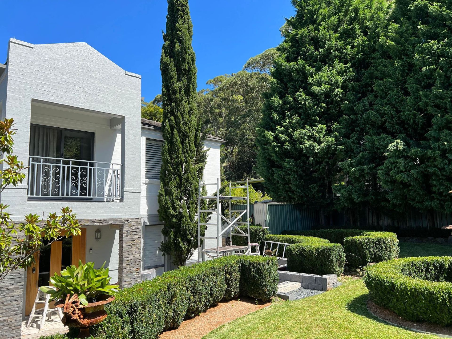 A white house with a balcony is surrounded by trees and bushes