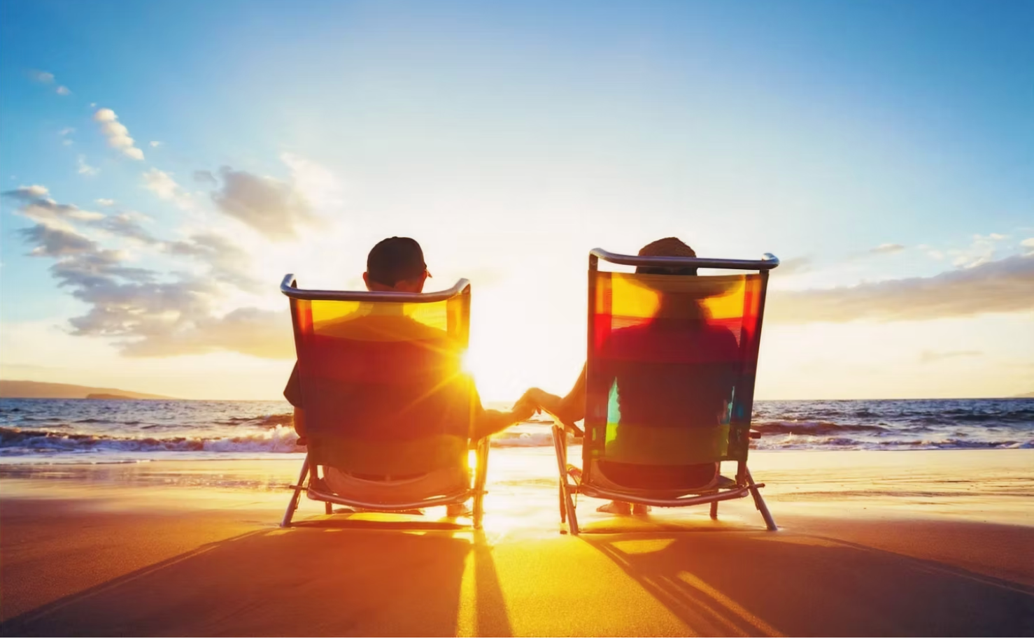 Two people sitting in beach chairs watching a sunset over the ocean